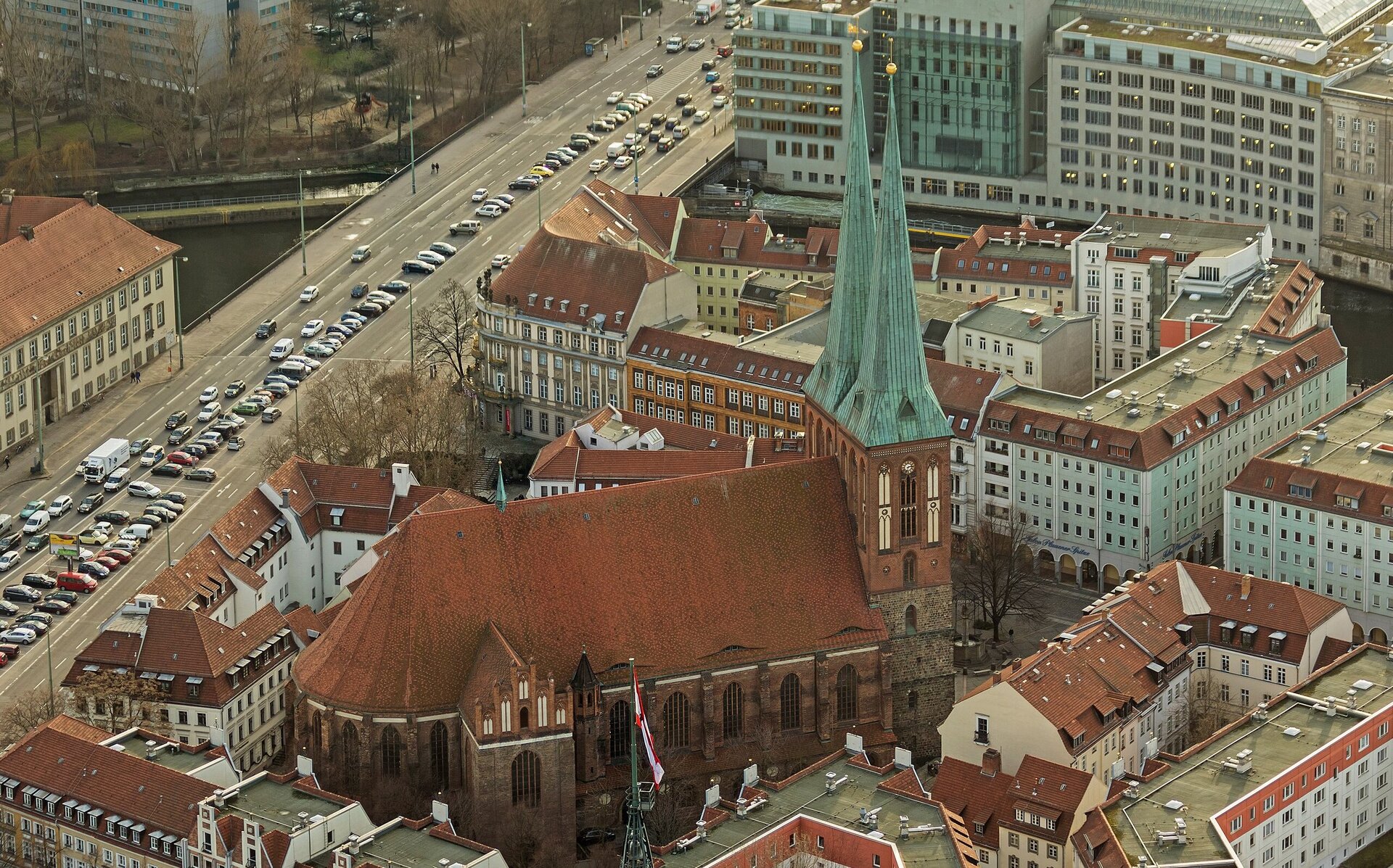 Eine Backsteinkirche mit rotem Dach und grünen Turmspitzen in einem Wohngebiet.