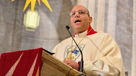Geistlichen in weiß-rotem liturgischem Gewand, der in einer Kirche am Pult steht und spricht.
